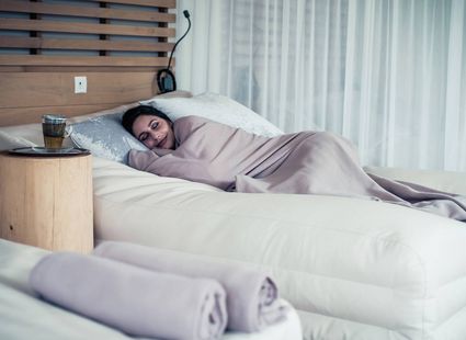 Una donna riposa su un lettino coperta da una coperta, accanto a una bevanda in una stanza spa tranquilla.