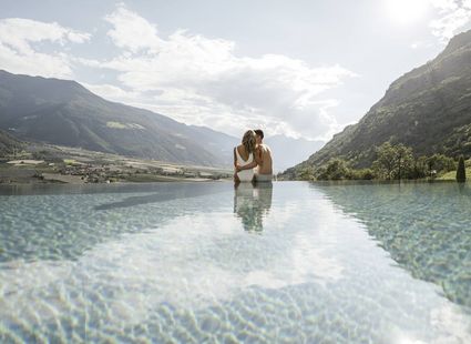 Ein Paar steht im Infinity-Pool mit Blick auf die Berge und das Tal.