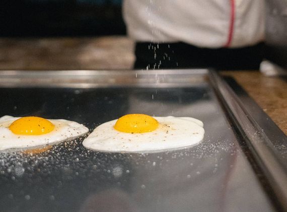 Ein Koch würzt zwei Spiegeleier auf einer heißen Grillplatte in der Gourmetküche.