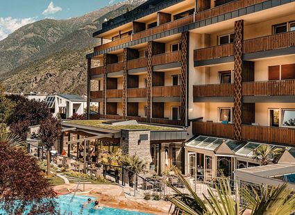 Außenansicht des Wellnesshotels Preidlhof mit Pool, Terrasse und Balkonen vor der Bergkulisse.