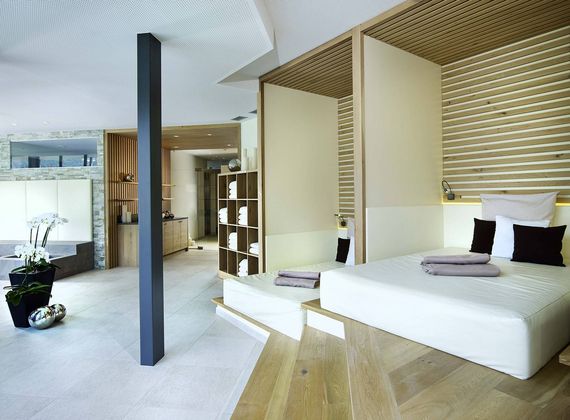 A bright wellness suite with a large bed, wooden slat details, and an open bathroom area.