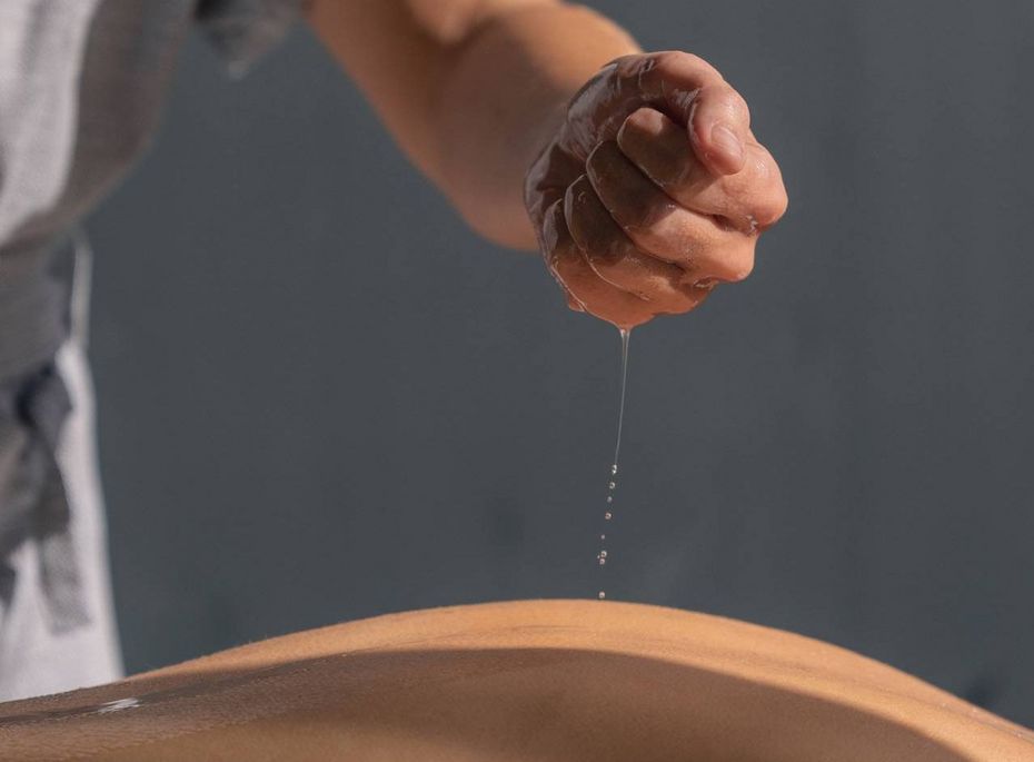 Massage im Preidlhof in Naturns Eine Masseurin tropft Öl auf den Rücken eines Gastes bei einer Massage.
