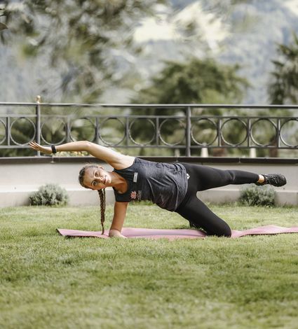 Eine Frau macht auf einer Matte im Garten eine seitliche Stützübung beim Fitness-Training.