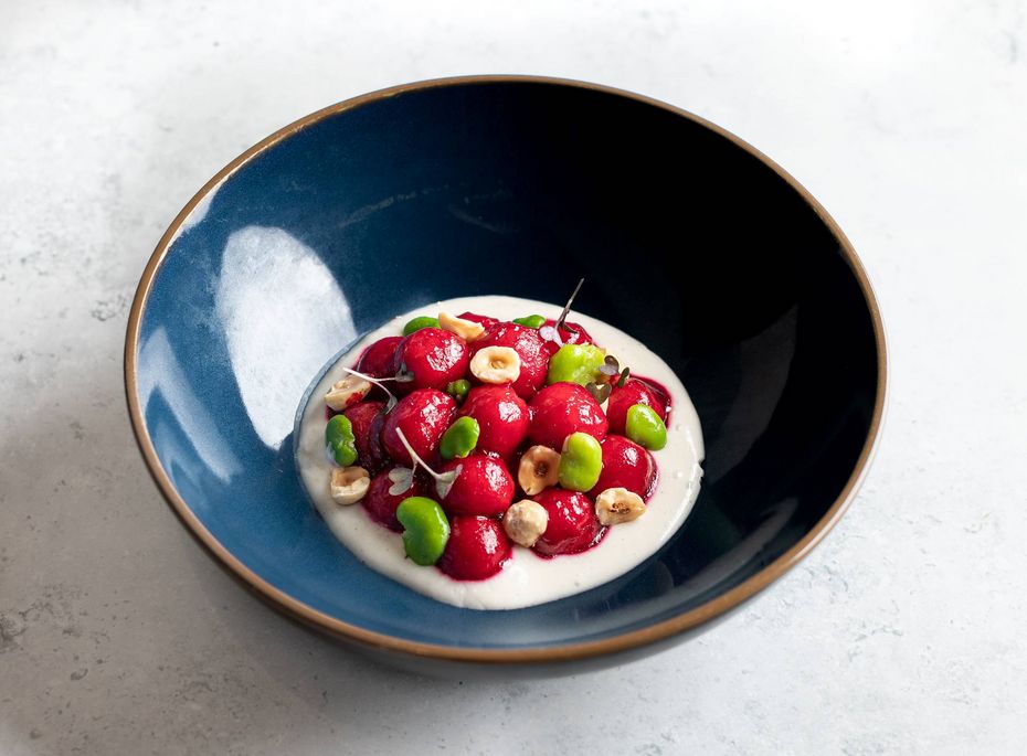 Dessert im Gourmethotel in Naturns Eine Dessertschale mit weißer Creme, roten Beeren, grünen Tupfen und Nüssen auf hellem Untergrund.