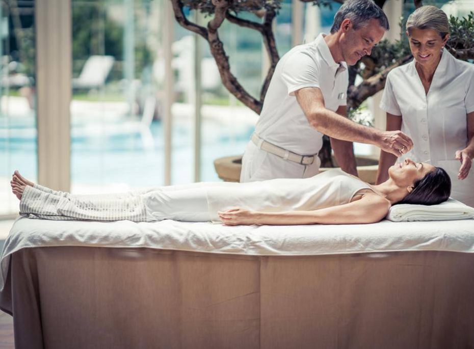 Ein Mann und eine Frau behandeln eine liegende Frau auf einer Liege im Spa-Bereich.