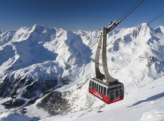 Eine rote Gondel der Bergbahn fährt vor einer schneebedeckten Alpenkulisse über die Hänge.
