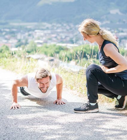 Ein Mann macht Liegestütze auf einem Weg, während eine Frau ihn beim Outdoor-Fitness-Training beobachtet.