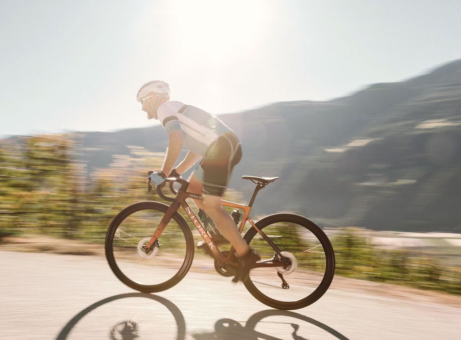 Rennradfahrer im Wellnesshotel Südtirol Ein Rennradfahrer fährt auf einer Straße vor Bergkulisse und sonnigem Licht.