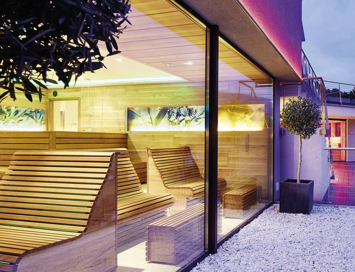 Wooden lounge benches beside a glass-walled sauna area at Preidlhof.