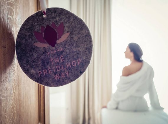 Eine Frau sitzt im Bademantel entspannt auf einer Liege im hellen Spa-Bereich des Preidlhof.