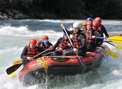 Eine Gruppe paddelt in einem Schlauchboot auf einem reißenden Fluss beim Rafting.