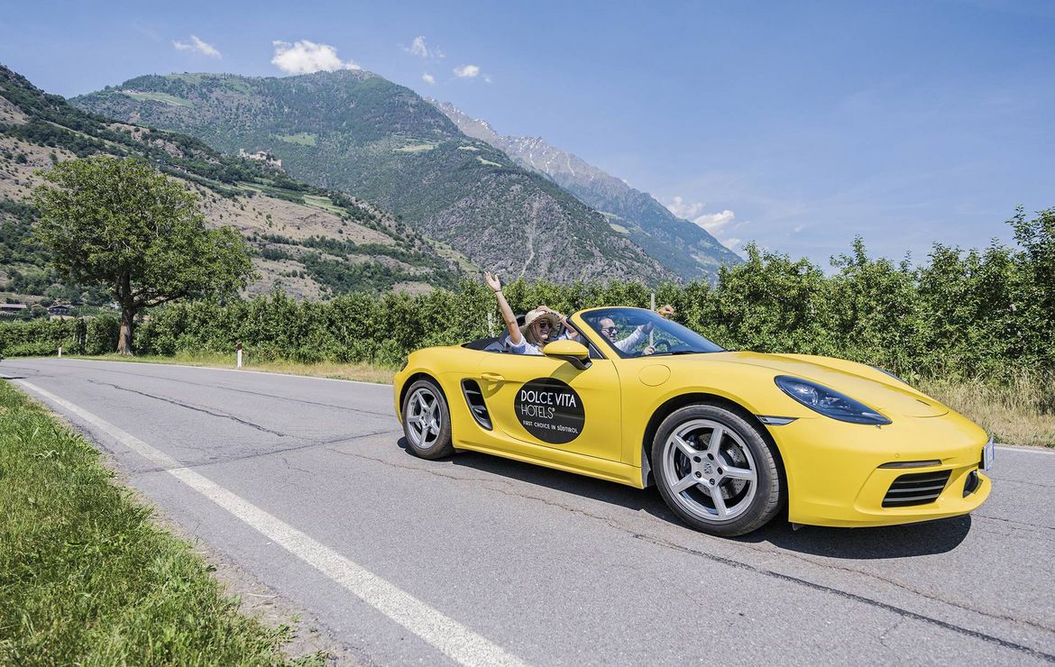 Ein gelber Cabrio-Sportwagen steht auf einer Landstraße vor einer Bergkulisse.