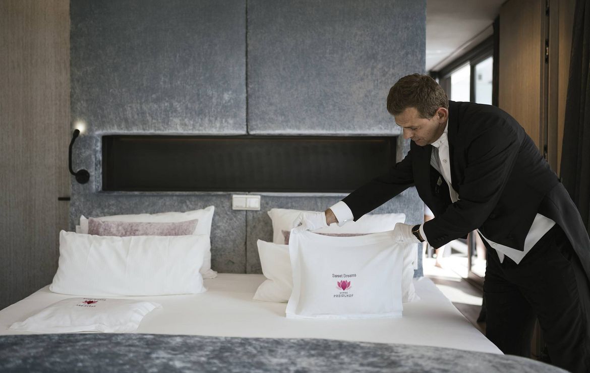 Ein Mitarbeiter richtet im Gästezimmer das Kissenmenü auf dem Bett her.