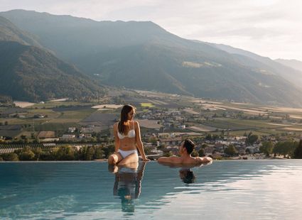 Ein Paar entspannt im Infinity-Pool mit Blick über das Tal und die Berge.