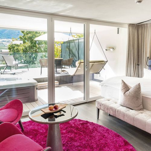 Eine helle Suite mit Bett, Sitzbereich und Terrasse mit Liegen und Bergblick.