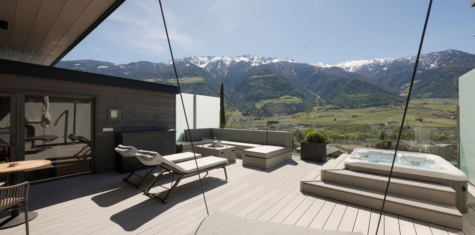 Die Terrasse der Penthouse Suite zeigt Liegen, Sitzmöbel und einen Whirlpool mit Bergblick.