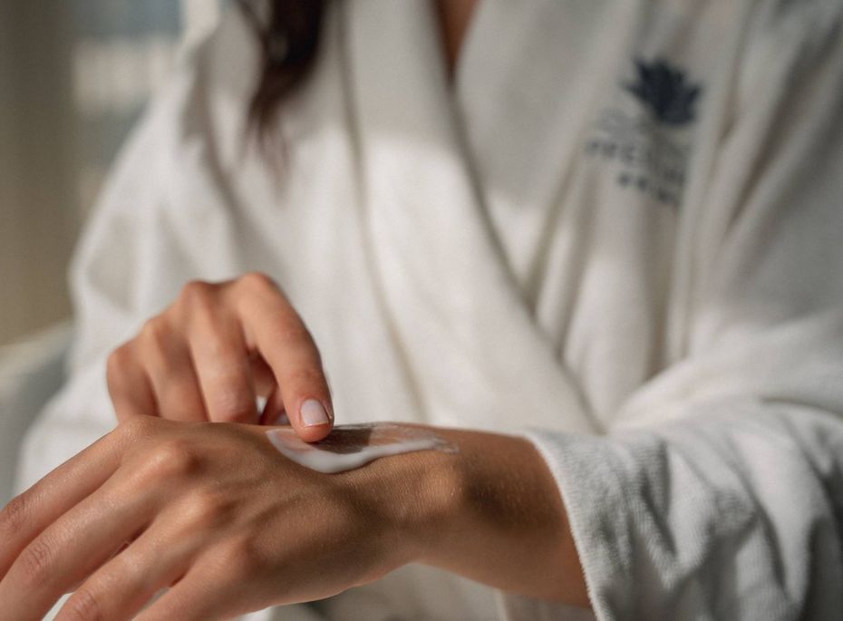 Wellnessbehandlung im Preidlhof in Naturns Eine Person im Bademantel trägt Creme auf die Hand auf.