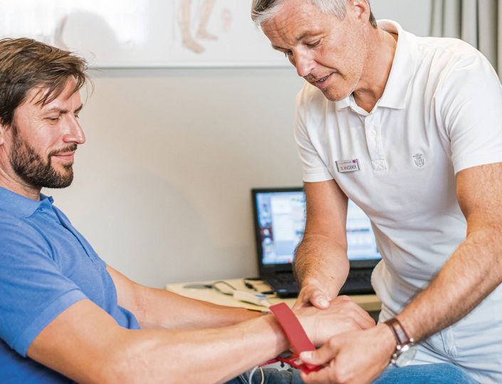 Ein Therapeut legt einem sitzenden Mann im Medical Spa ein rotes Band um das Handgelenk.