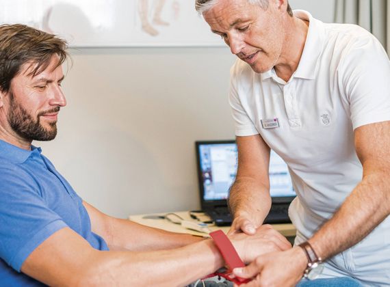 Ein Therapeut legt einem sitzenden Mann im Medical Spa ein rotes Band um das Handgelenk.