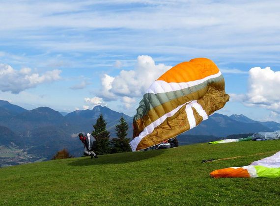 Ein Paraglider bereitet den Start auf einer Wiese mit Blick auf die Berge vor.