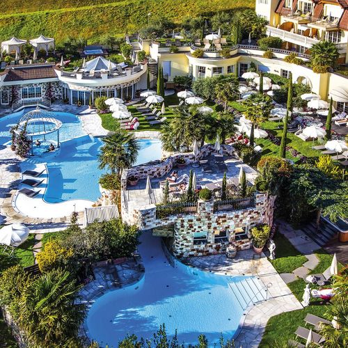 Eine weitläufige Poollandschaft mit mehreren Becken, Liegen, Palmen und Sonnenschirmen vor dem Hotelgebäude.