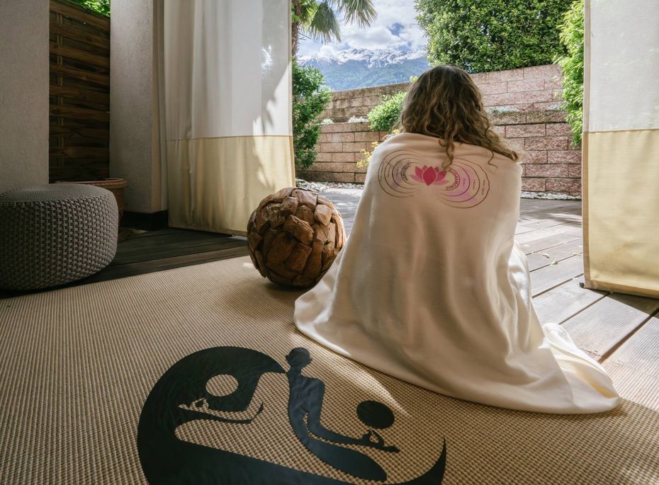 Eine Person sitzt in einem Ruheraum mit Blick ins Freie auf Terrasse und Garten.