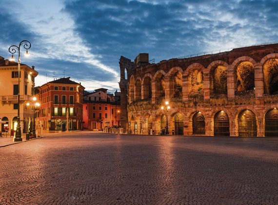Die römische Arena von Verona steht neben historischen Gebäuden an einem leeren Platz in der Abenddämmerung.