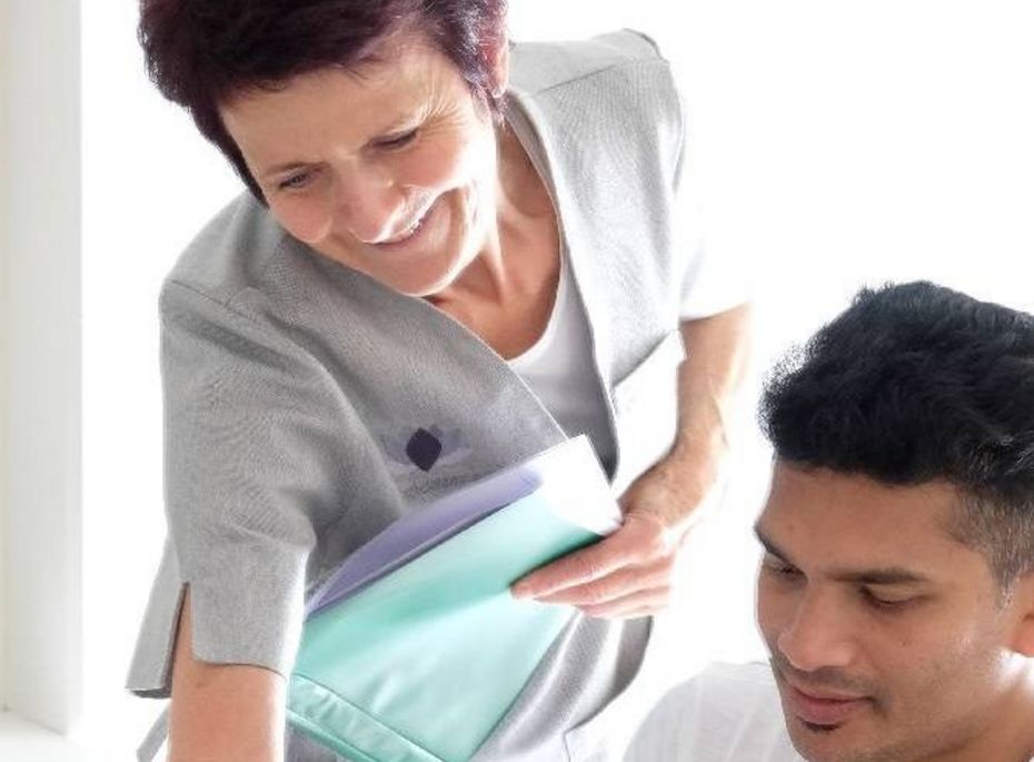 Wellnessbehandlung im Preidlhof mit Betreuung Eine Mitarbeiterin begleitet einen Gast bei einer Wellnessbehandlung und reicht ihm Unterlagen.