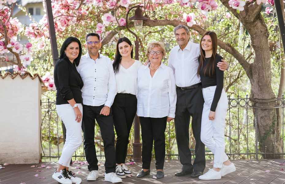 Preidlhof Team im Frühlingsgarten Sechs Mitarbeitende von Preidlhof stehen lächelnd unter blühenden Bäumen im Garten.