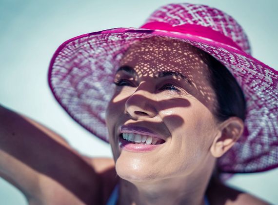 A smiling woman in a pink sun hat relaxes outdoors in bright sunlight.