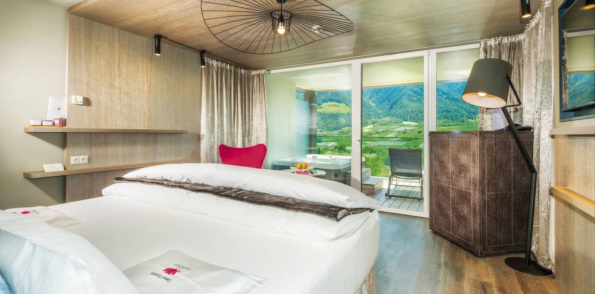 A modern luxury suite with a double bed, balcony doors, and mountain views.
