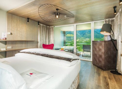 A modern luxury suite with a double bed, balcony doors, and mountain views.
