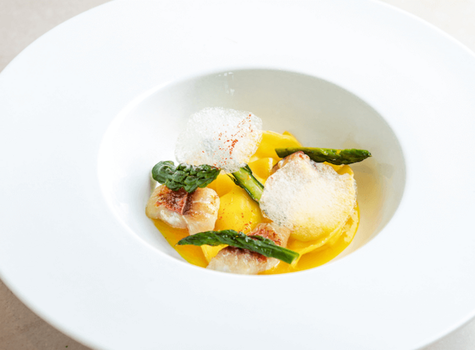 Gourmetgericht mit Pasta und Spargel im Preidlhof Ein angerichtetes Gourmetgericht mit Pasta, grünem Spargel und hellen Toppings in einer tiefen weißen Schale.
