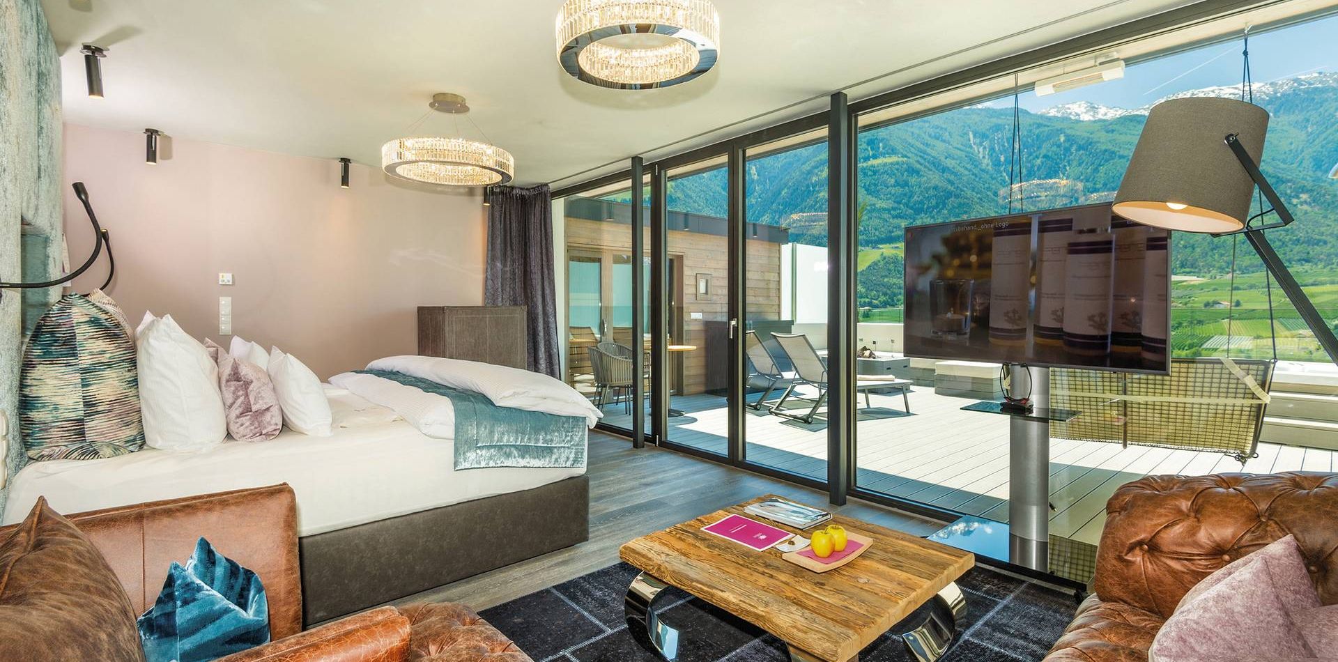 Die Penthouse Suite mit Bett, Sofas, Fernseher und großer Glasfront mit Blick auf die Berge.