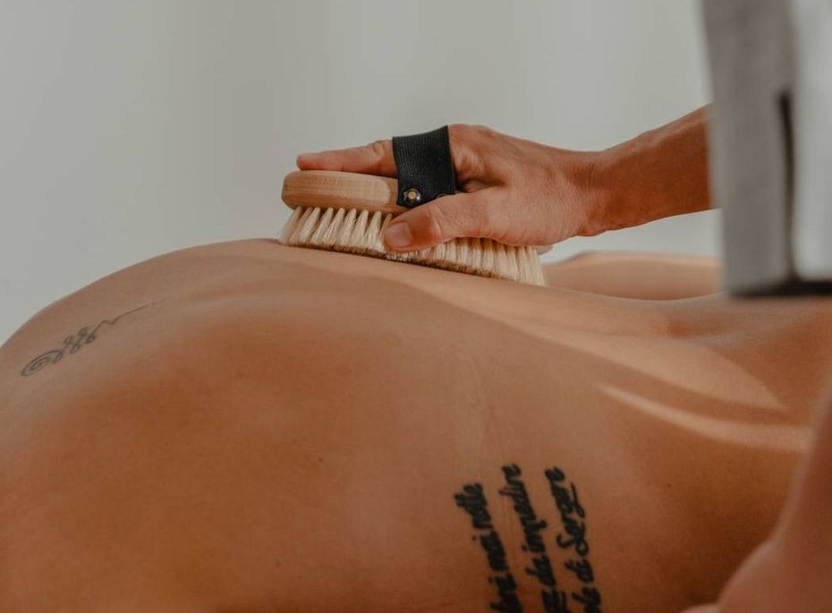 Massage im Wellnesshotel Preidlhof in Naturns Eine Person erhält in einem Wellnessraum eine Bürstenmassage auf dem Rücken.