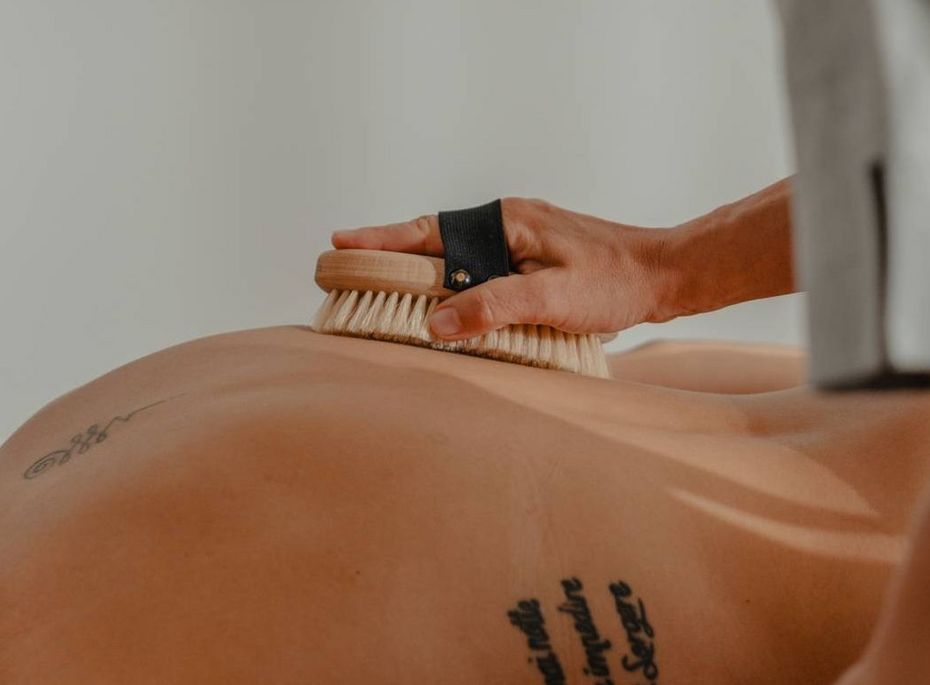 Massage im Wellnesshotel Preidlhof in Naturns Eine Person erhält in einem Wellnessraum eine Bürstenmassage auf dem Rücken.