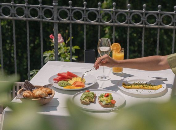 Auf der Terrasse stehen ein gedeckter Tisch mit Gourmetfrühstück, Brot, Obst, Säften und weiteren kleinen Speisen.