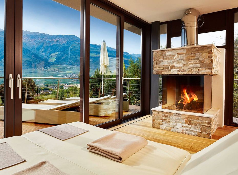 Wellnesssuite mit Kamin und Bergblick im Preidlhof Eine helle Wellnesssuite mit Kamin, großer Glasfront und Blick auf die Berge sowie den See.