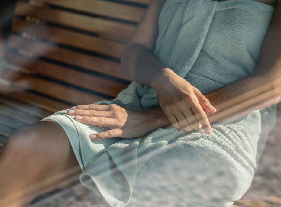Sauna-Entspannung im Wellnesshotel in Naturns Eine Person sitzt in ein Handtuch gewickelt in einer Sauna mit Holzbank.