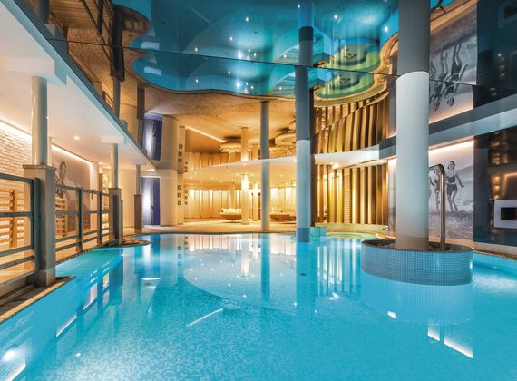 A bright indoor pool with calm turquoise water and curved ceilings inside the spa area.