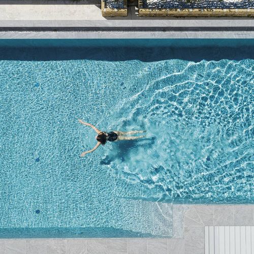 Eine Person schwimmt im türkisfarbenen Pool mit hellen Steinrändern und sichtbaren Wasserreflexen.