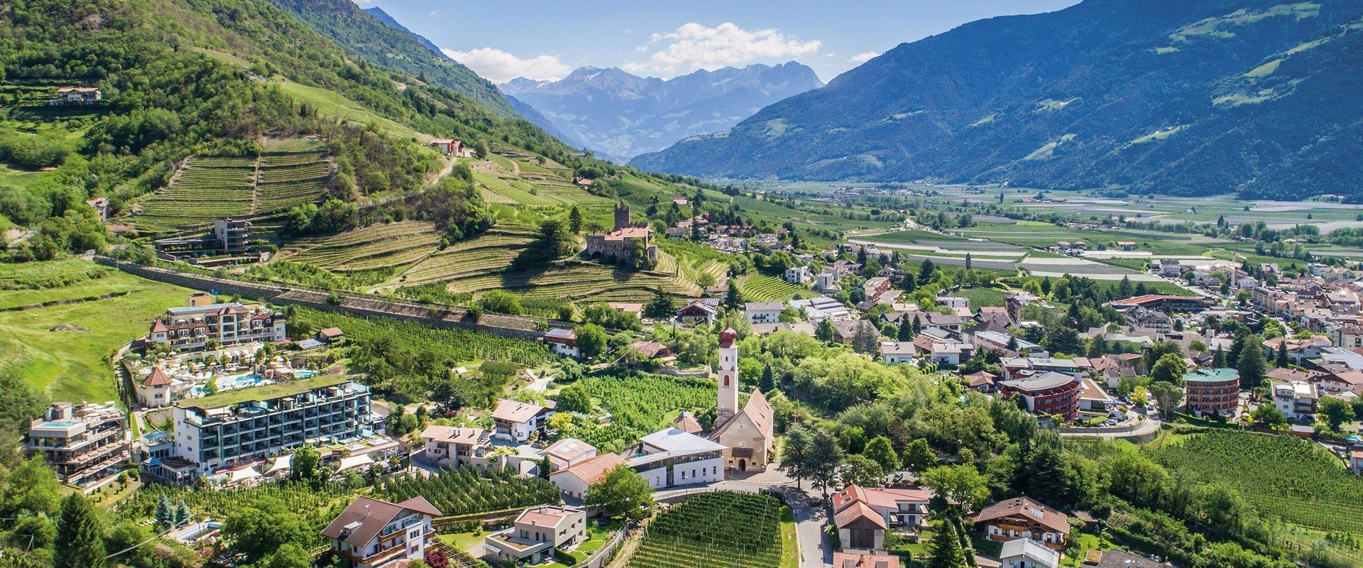 A panoramic view shows Naturns, a church, vineyards and green hills stretching into the South Tyrol valley.