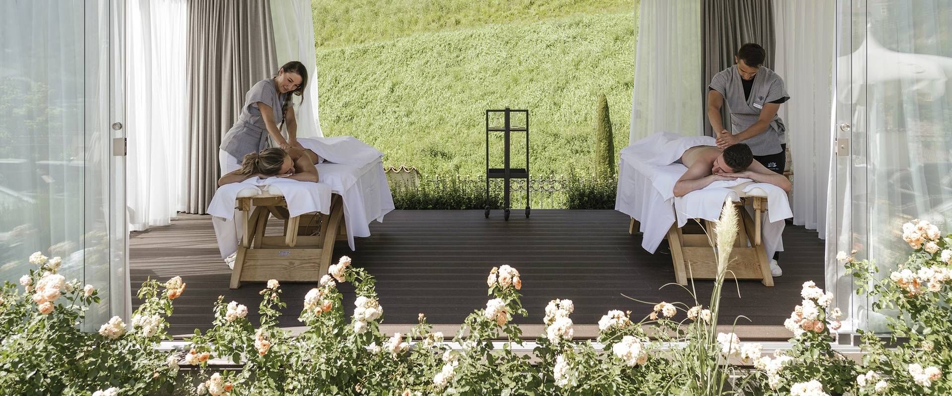 Zwei Spa-Behandlungen unter einem offenen Pavillon mit Blick auf die grüne Gartenfläche.