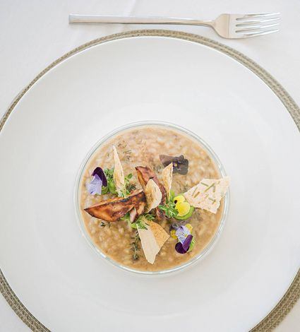 Ein fein angerichtetes Gourmetgericht in einer Schale auf einem großen weißen Teller mit Besteck.