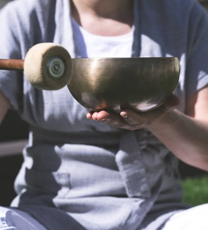A person holds a singing bowl while striking it with a mallet during a spa treatment session.