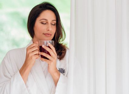 Eine Frau im Bademantel hält in einem Wellnesshotel eine Tasse Tee und hat die Augen geschlossen.