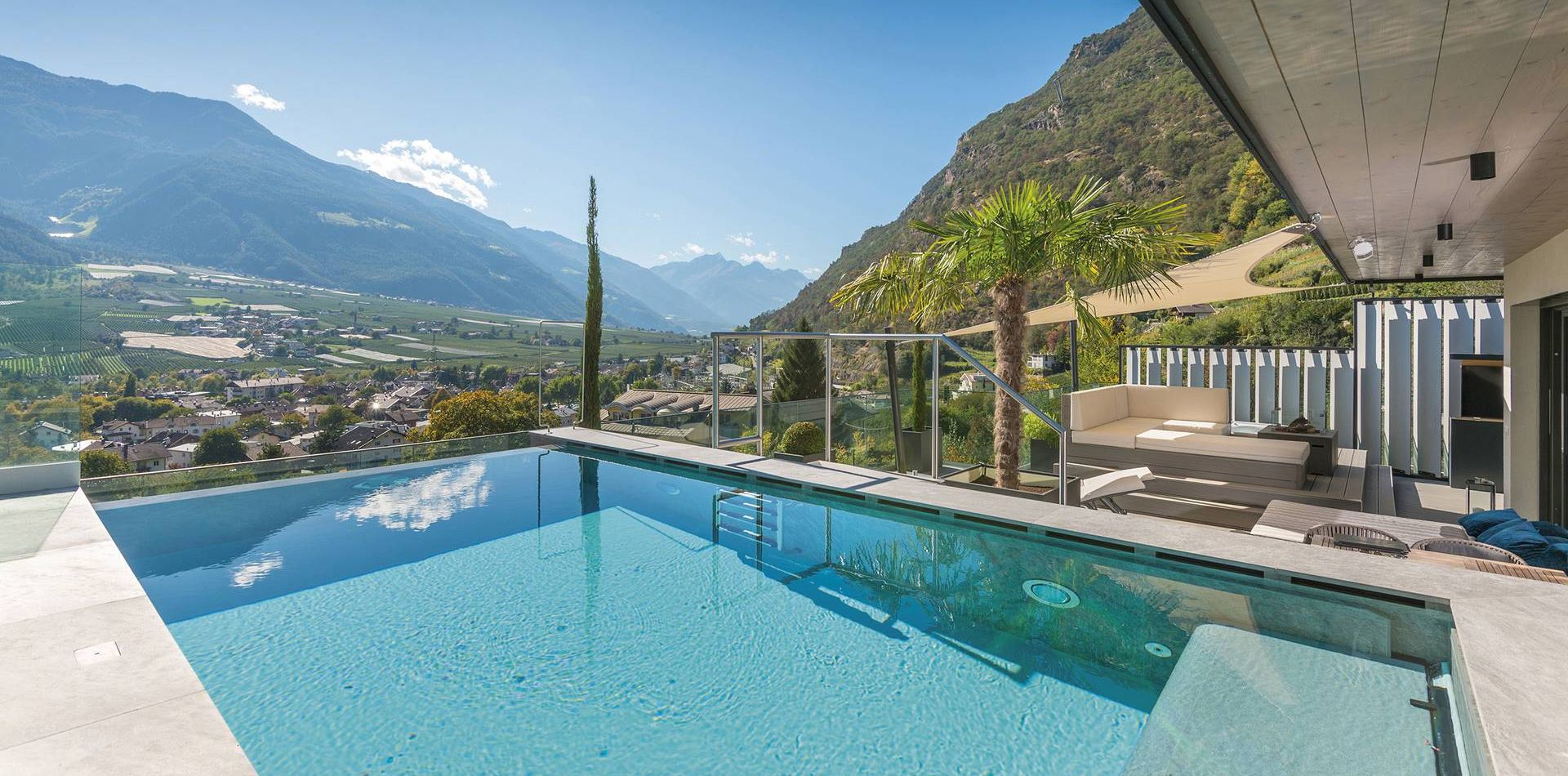 Una piscina a sfioro accanto a una terrazza con salotto si affaccia sulla valle e sulle montagne.