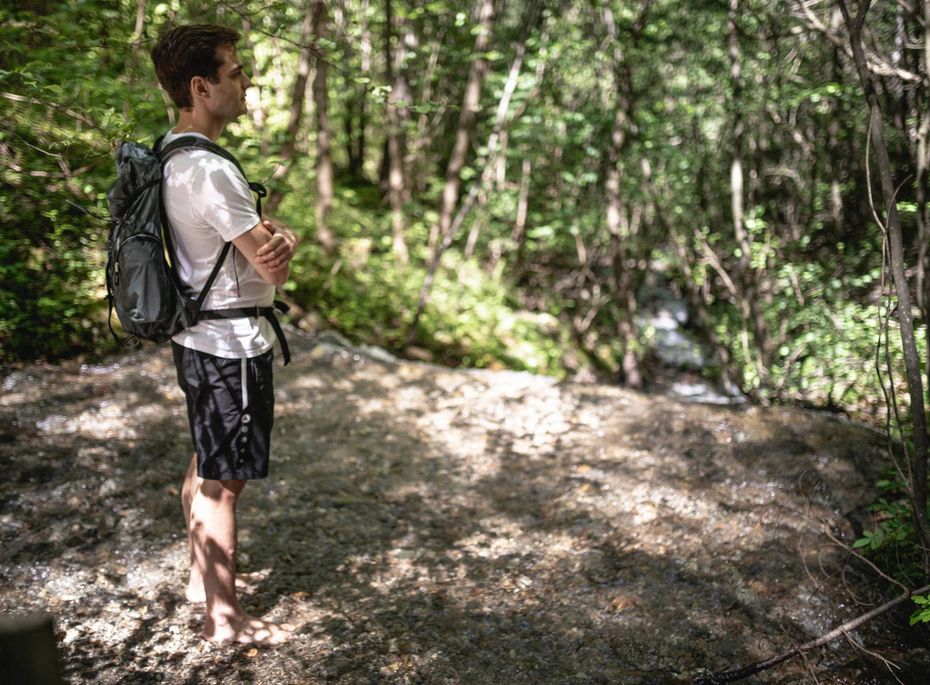 Ein Mann mit Rucksack steht auf einem Waldweg und blickt in Richtung der Bäume.