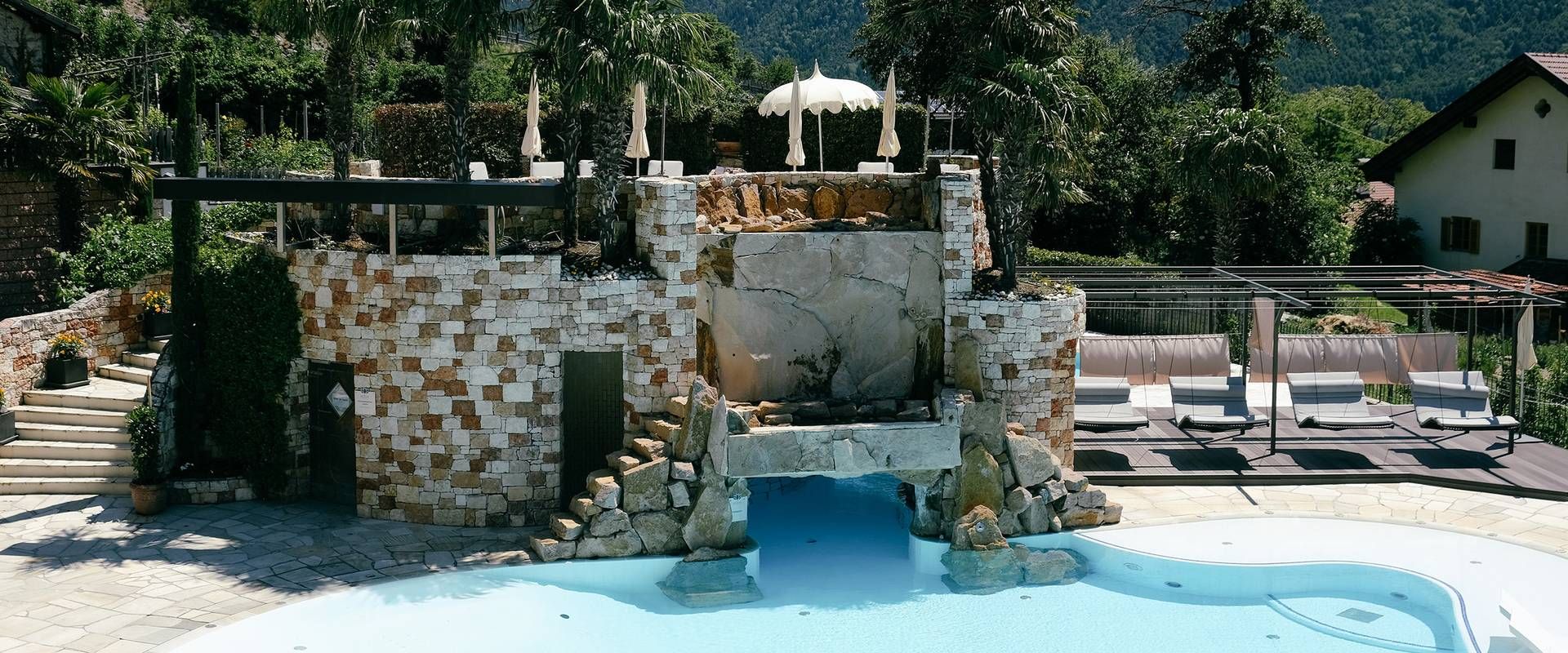 An outdoor wellness pool with a stone water feature and sun loungers beside it.