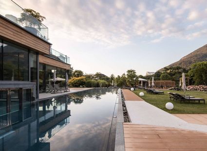 Der Infinity-Pool liegt neben der modernen Hotelanlage mit Liegewiese und Bergblick.